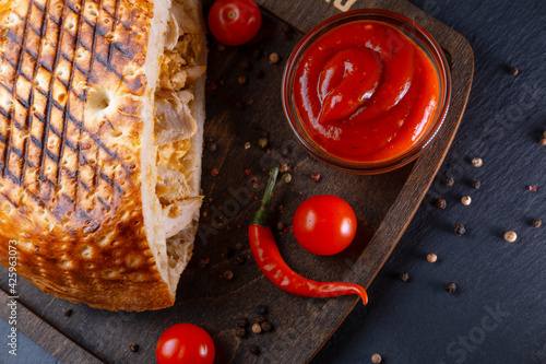 Turkish shawarma with chicken in a flatbread on a tandoor, cooked on a barbecue, on a wooden board with chili peppers and cherry tomatoes on a dark background.