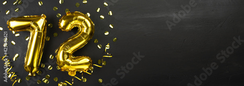 golden foil balloon number seventy two. Birthday or anniversary card with the inscription 72. Black concrete background. Anniversary celebration. Banner.