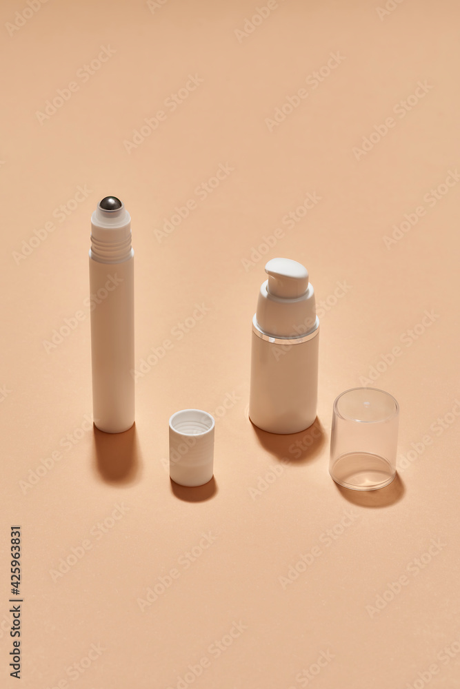 White plastic pump bottle and tube for eye roller skin care product isolated over beige background with reflection White plastic pump bottle and tube for eye roller skin care product isolated over beige background with reflection
