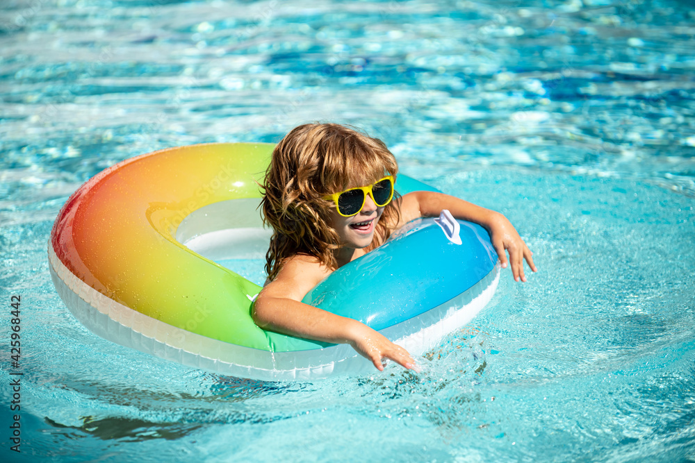 Summertime vacation. Summer kids weekend. Funny boy in swiming pool on inflatable rubber circle at aquapark.