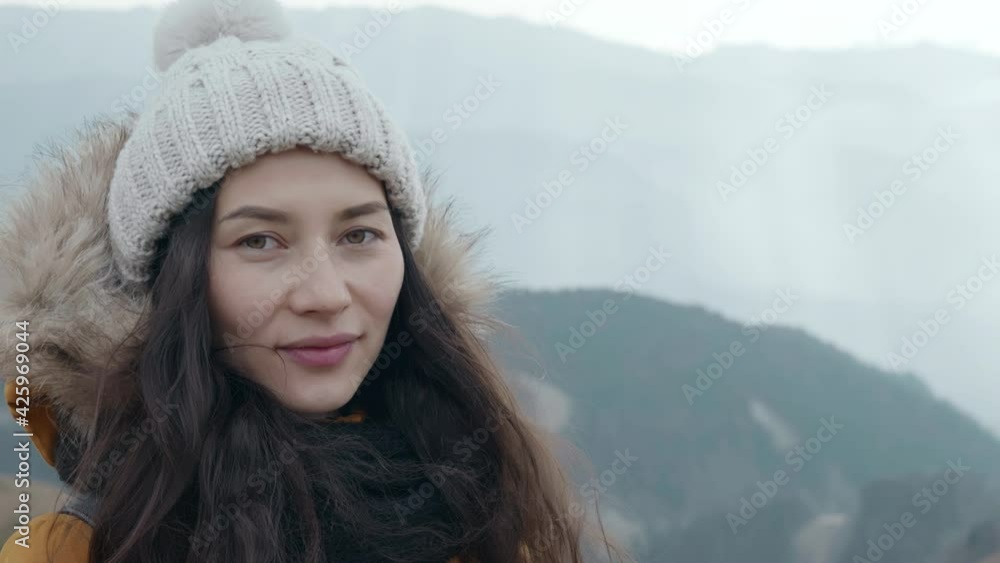 Young hiker at amazing hazy background of mountain landscape in smoke. Portrait of asian woman tourist enjoys breathing fresh air high in cloudy mountains at cold weather. Concept of active lifestyle Young hiker at amazing hazy background of mountain landscape in smoke. Portrait of asian woman tourist enjoys breathing fresh air high in cloudy mountains at cold weather. Concept of active lifestyle