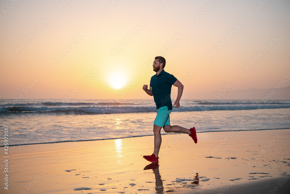 Full length of healthy man running and sprinting outdoors. Male runner. Man running on the beach at sunset. Healthy lifestyle concept.