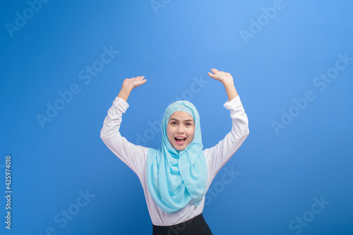 Portrait of a young muslim woman with hijab over blue background studio.