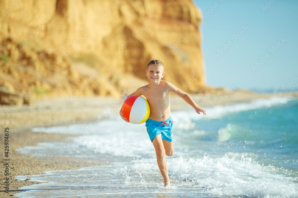 Naklejka premium Boy child has fun at sea. Summer, happiness, sea and a child with a ball. High quality photo.