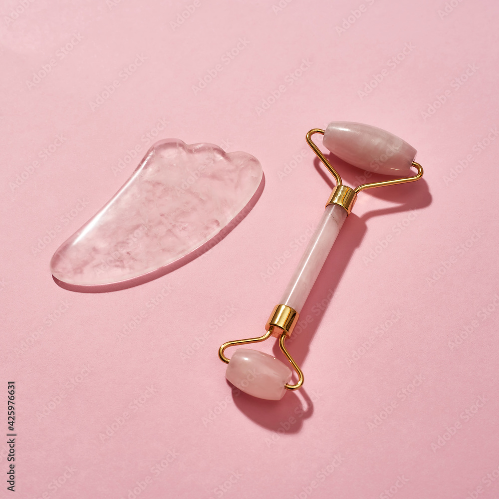Rose quartz facial massage tools, face roller and Gua Sha scraper isolated over pink background