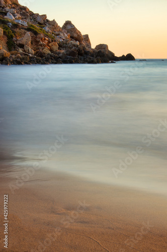 Sandy beach next to smooth blue water and cliffs at Golden Bay on a warm fall evening.