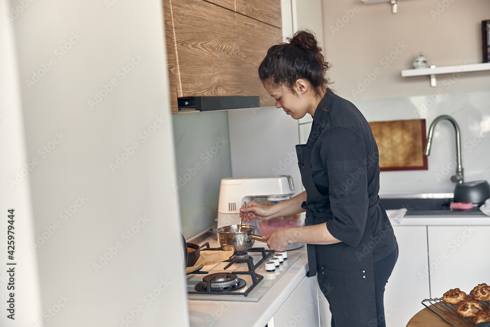 Professional confident woman is preparing custard cakes at light modern kitchen at home Professional confident woman is preparing custard cakes at light modern kitchen at home