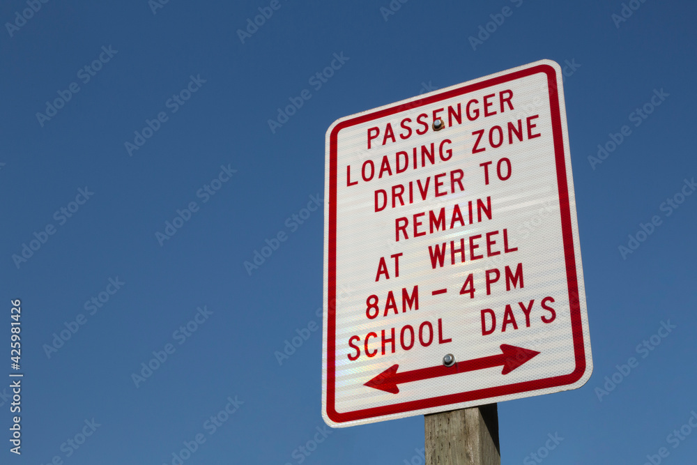 School Days Passenger Loading Zone, Driver to Remain at Wheel sign with clear blue sky background School Days Passenger Loading Zone, Driver to Remain at Wheel sign with clear blue sky background