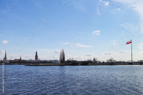 City view of the Old Town of Riga from the other side of the Daugava River with the national flag of the Republic of Latvia
