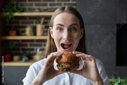 Hungry woman eating a hamburger sitting in the kitchen
