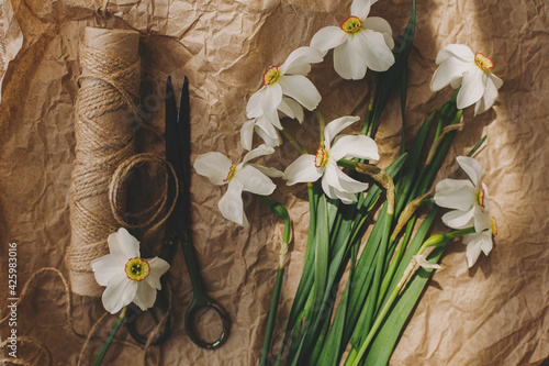 Stylish spring flowers rural still life. Daffodils, scissors, twine in sunny light on rustic paper