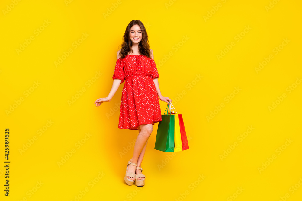 Full length photo of charming cheerful girl standing hand hold bags beaming smile isolated on yellow color background