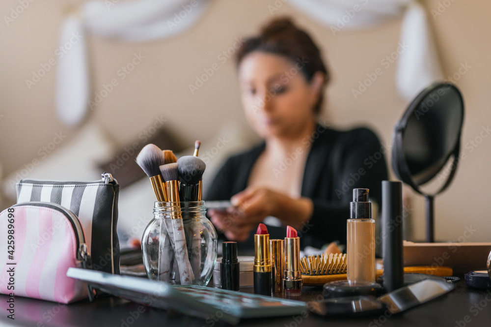 Lipsticks and makeup brushes on a wooden table, in the background a woman putting on makeup