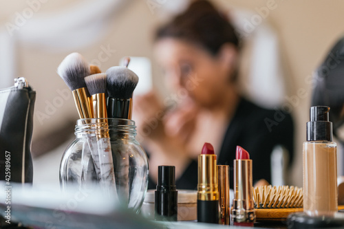 Lipsticks on a wooden table and in the background a woman putting on makeup photo