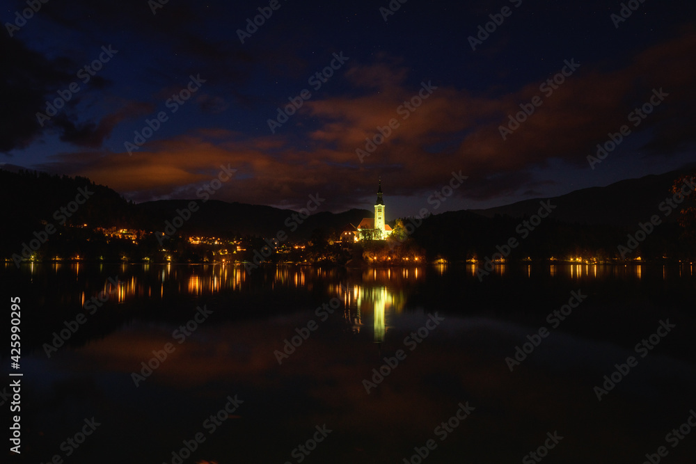 Famous alpine Bled lake (Blejsko jezero) in Slovenia, amazing night landscape. Scenic view of the lake, island with church in lights, mountains and blue sky with clouds, outdoor travel background