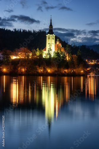 Famous alpine Bled lake (Blejsko jezero) in Slovenia, amazing night landscape. Scenic view of the lake, island with church in lights, mountains and blue sky with clouds, outdoor travel background