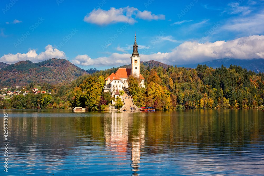 Famous alpine Bled lake (Blejsko jezero) in Slovenia, amazing autumn landscape. Scenic view of the lake, island with church, blue sky with clouds and reflection in the water, outdoor travel background