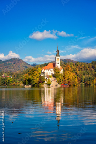 Famous alpine Bled lake (Blejsko jezero) in Slovenia, amazing autumn landscape. Scenic view of the lake, island with church, blue sky with clouds and reflection in the water, outdoor travel background