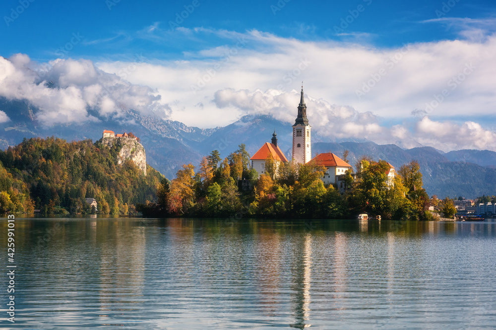 Famous alpine Bled lake (Blejsko jezero) in Slovenia, amazing autumn landscape. Scenic view of the lake, island with church, Bled castle, mountains and blue sky with clouds, outdoor travel background