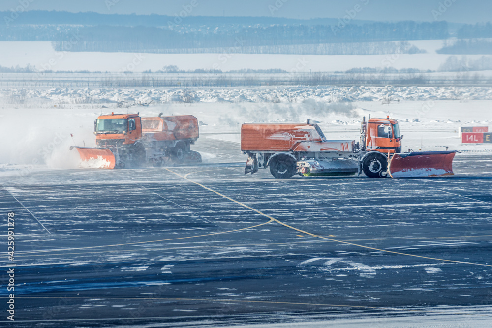 Snowplow trucks clear snowdrifts after a heavy storm blizzard at winter airport. The concept of changing weather conditions and flight delays