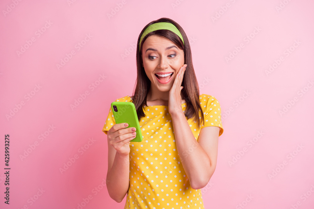 Photo of young happy smiling cheerful beautiful girl hold hand cheek see good comment in phone isolated on pink color background Photo of young happy smiling cheerful beautiful girl hold hand cheek see good comment in phone isolated on pink color background