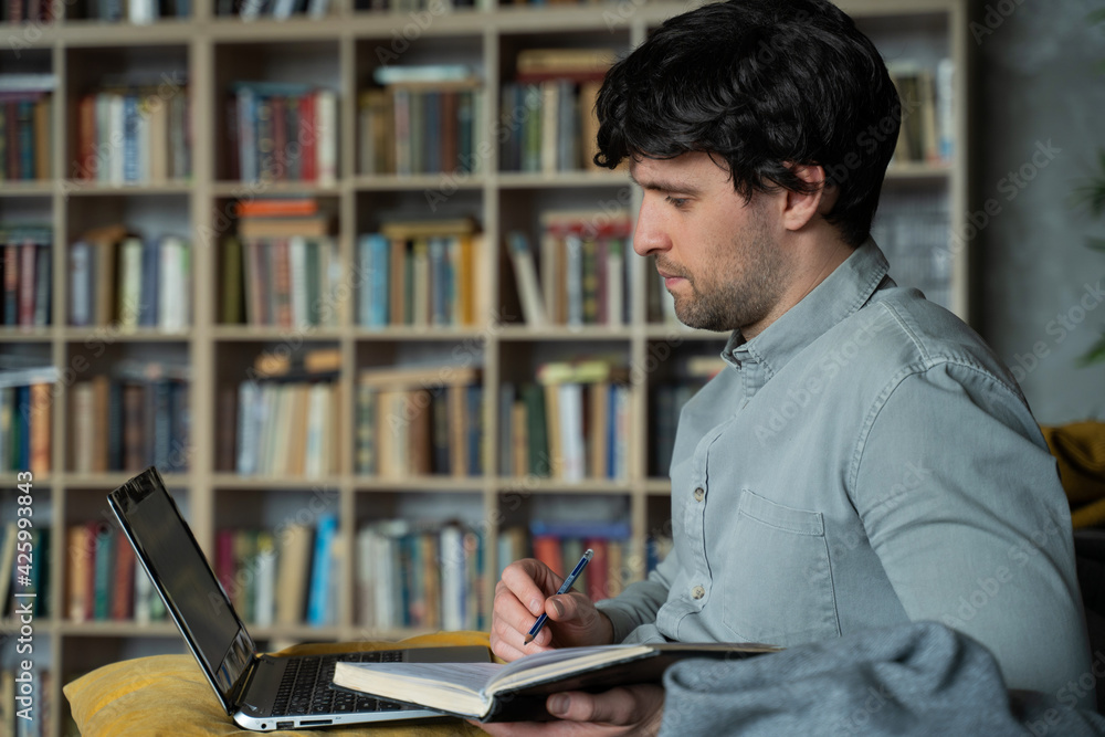 Portrait of a man sitting on a sofa with a laptop on the background of a bookshelf