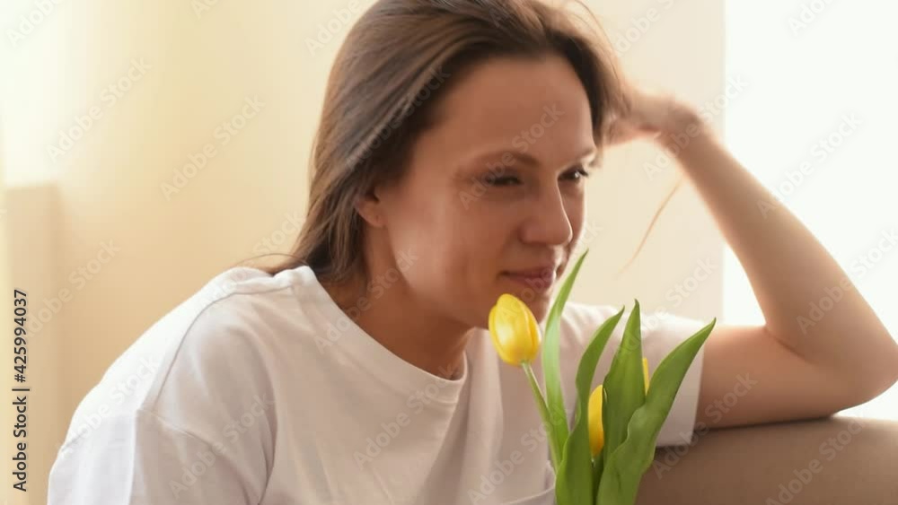 Attractive caucasian woman smiles and enjoys the scents of yellow tulips in the home interior.Mother's day, 8 March and Birthday concept.Close up, slow motion. Attractive caucasian woman smiles and enjoys the scents of yellow tulips in the home interior.Mother's day, 8 March and Birthday concept.Close up, slow motion.