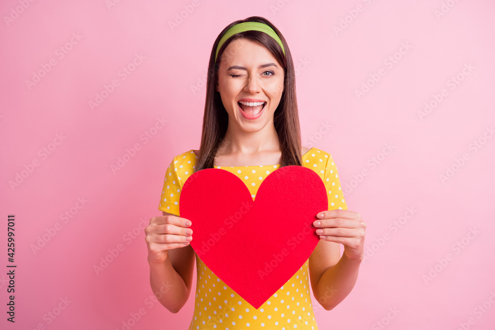 Photo of young attractive cheerful smiling good mood girl wink eye hold big red heart isolated on pink color background Photo of young attractive cheerful smiling good mood girl wink eye hold big red heart isolated on pink color background