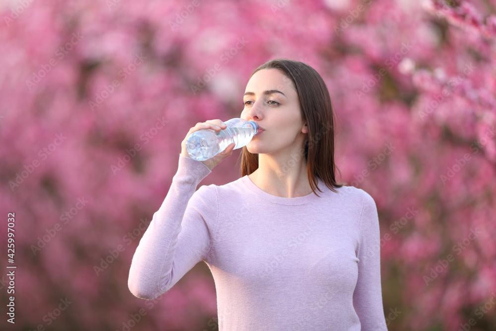 Woman drinking water from bottle in a flowered field Woman drinking water from bottle in a flowered field