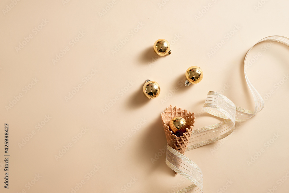 Ice cream waffle cone with ribbon and balls ornament topping. Skin color background Ice cream waffle cone with ribbon and balls ornament topping. Skin color background