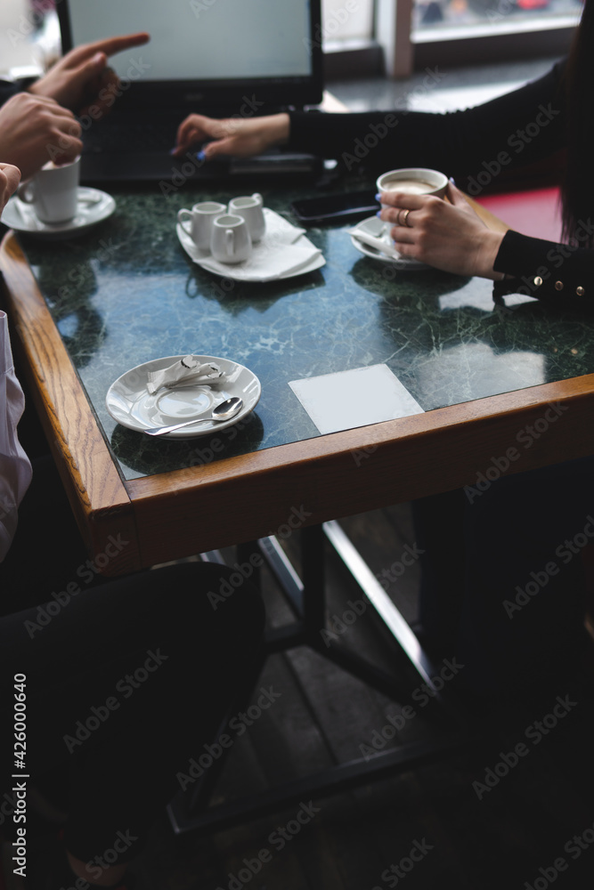 meeting in a cafe for a cup of coffee. laptop on the table. Conversation and discussion. Business and work concept. Without the visibility of faces. Vertical photo