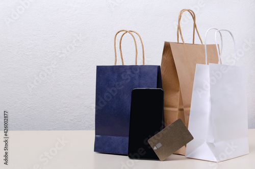 Shopping bags and credit card, blank screen of smartphone on the bright surface against white wall.Empty space