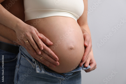 Man touching his pregnant wife's belly on light background, closeup © New Africa