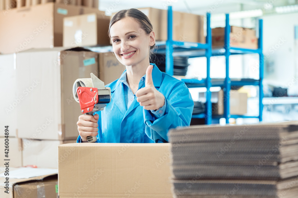 © Kzenon - Woman in factory warehouse packaging goods giving thumbs-up
