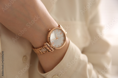 Woman with luxury wristwatch on light background, closeup photo