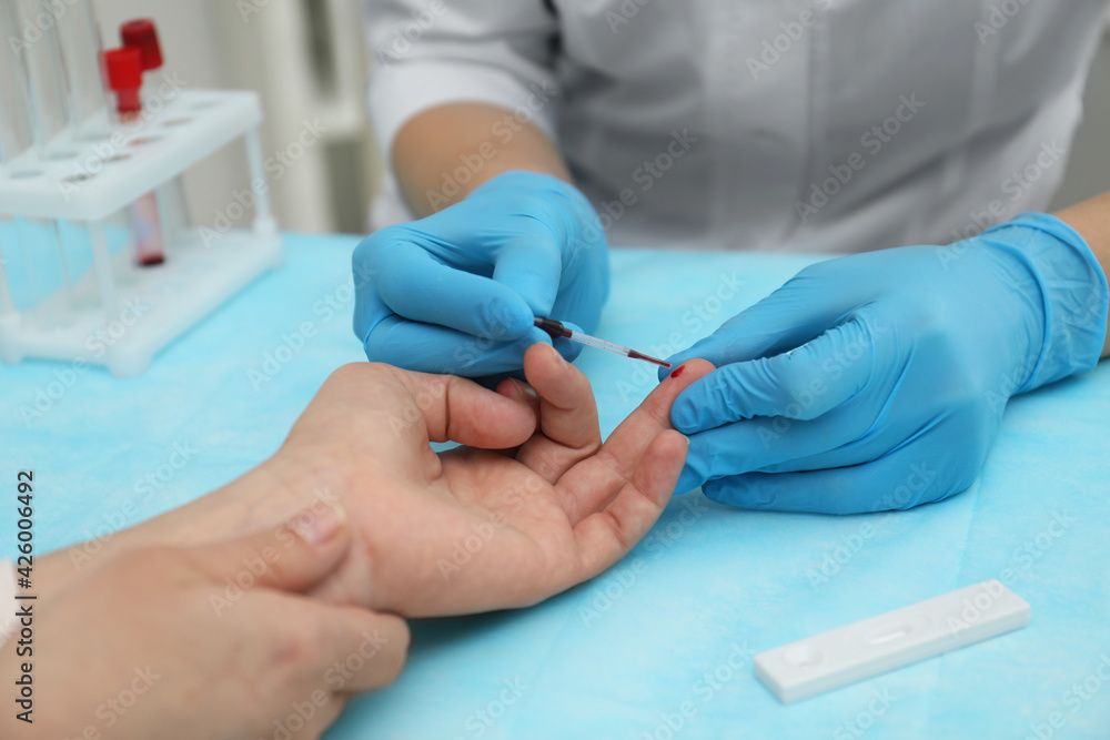 Doctor taking blood sample from patient's finger at table in clinic, closeup Doctor taking blood sample from patient's finger at table in clinic, closeup