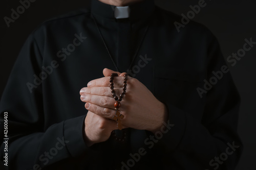 Priest with beads praying on dark background, closeup