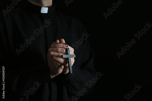 Priest with cross on dark background, closeup. Space for text photo