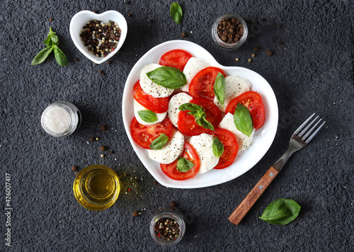 Caprese salad. Italian salad with fresh tomatoes, mozzarella cheese and basil on a dark background. Top view.