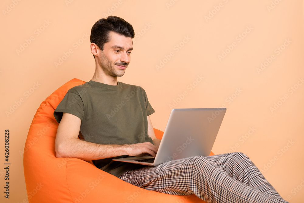 Photo of young happy positive good mood businessman sit armchair working in laptop isolated on beige color background Photo of young happy positive good mood businessman sit armchair working in laptop isolated on beige color background