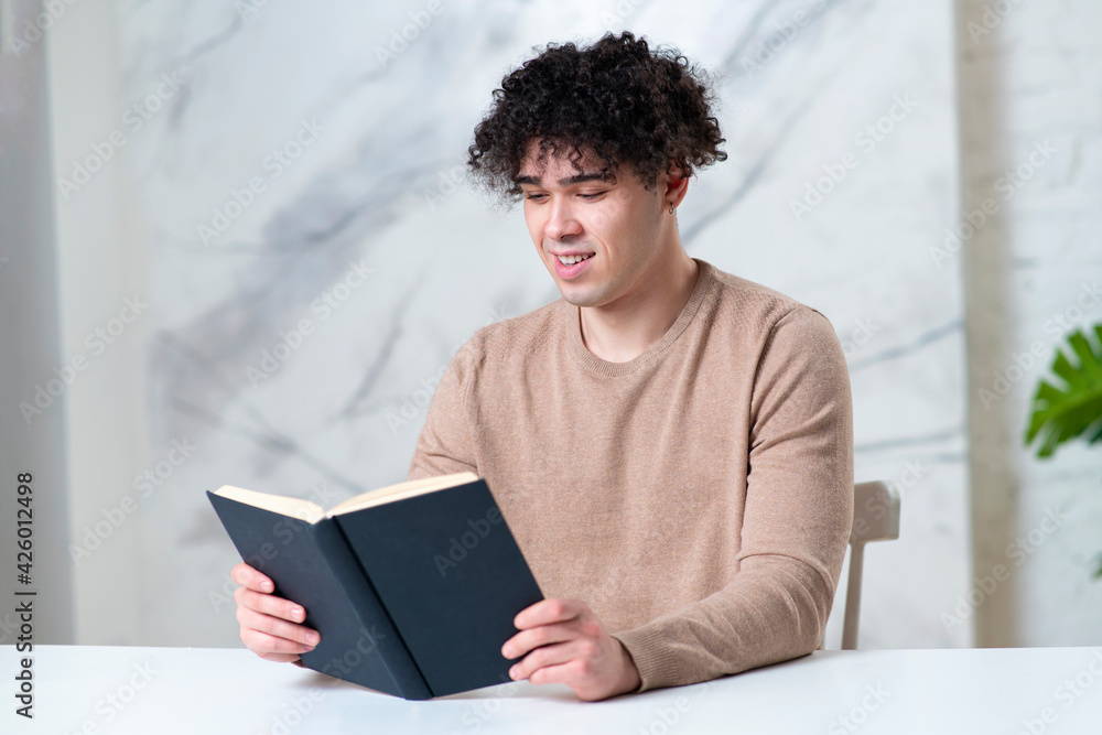 Portrait of happy positive intelligent Latino guy student, young handsome ethnic man reader is reading interesting book, sitting at table at home and smiling. Education, intelligence concept Portrait of happy positive intelligent Latino guy student, young handsome ethnic man reader is reading interesting book, sitting at table at home and smiling. Education, intelligence concept
