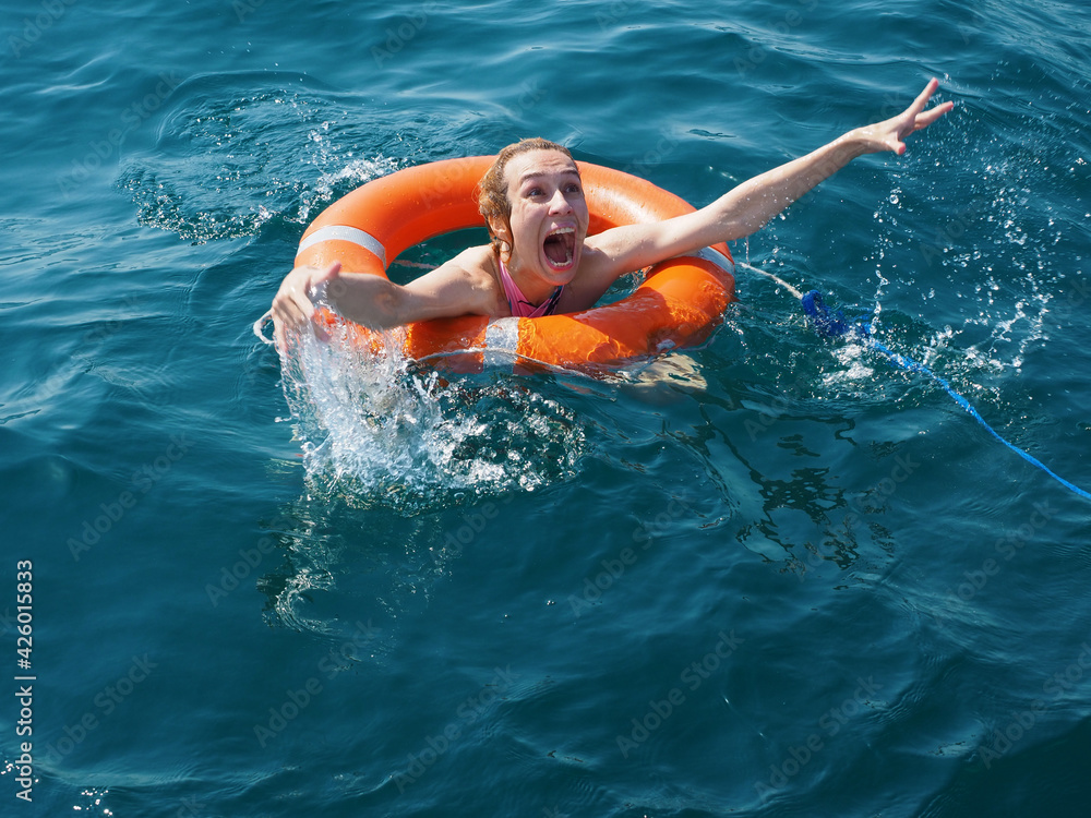 Scared screaming drowning girl in orange lifebuoy in the open blue sea