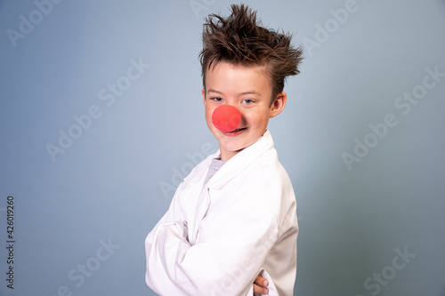 cool young schoolboy with wild hair posing with red clown nose on blue background and is happy © epiximages