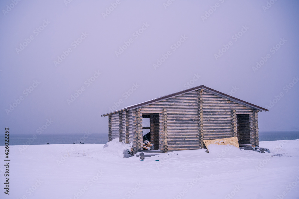 The wooden house in winter has a lonely atmosphere. The location is on the coast of the Barents Sea in Russia.