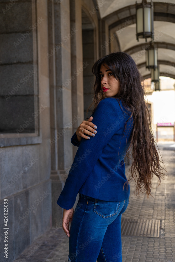 Fototapeta premium Young woman posing for a portrait holding her shoulder. She wears jeans and an blue American jacket. The photo was taken in La Laguna, Tenerife.