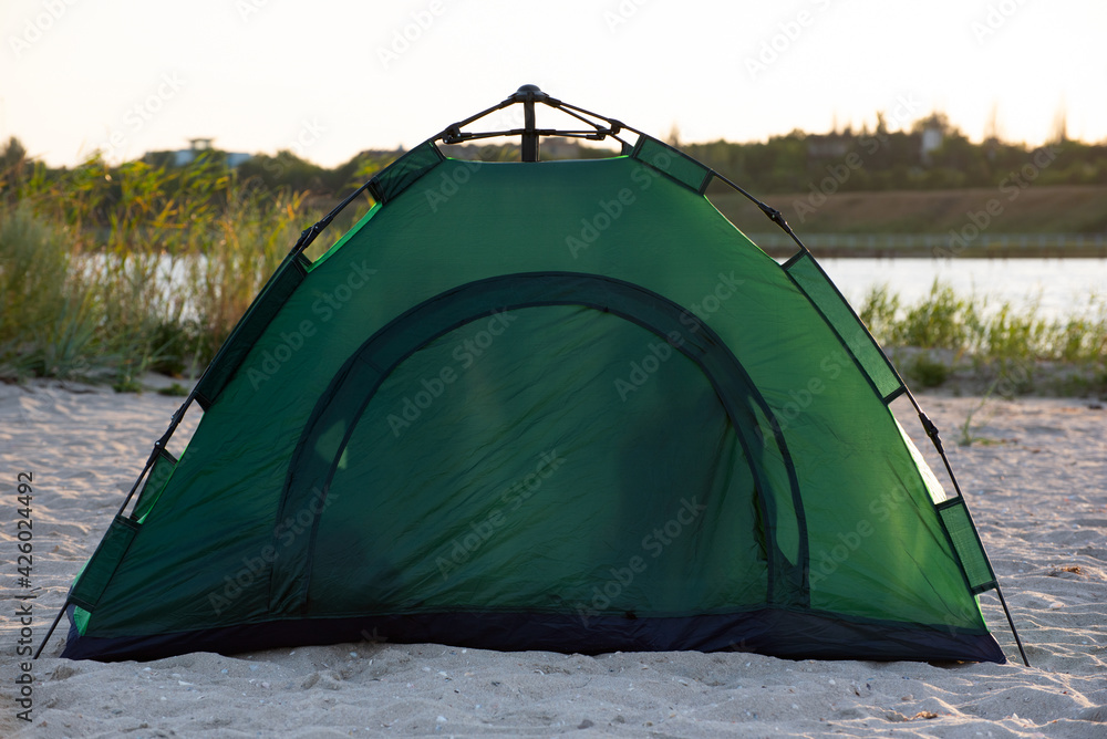 Green tourist tent on the river bank. Tourist equipment