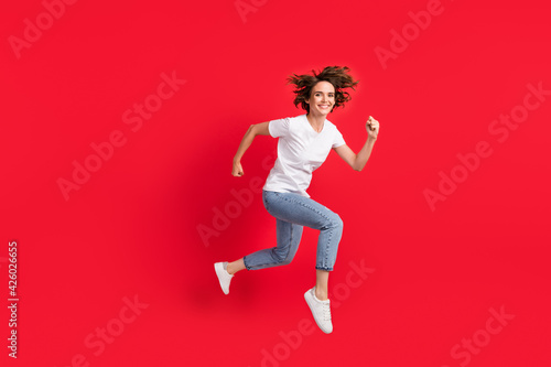 Full length body size view of attractive cheerful girl jumping running action isolated over bright red color background