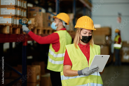 Caucasian female worker checking the order inside a warehouse while wearing a face mask - Face focus