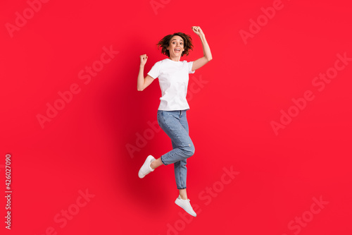 Full length body size view of attractive cheerful skinny girl jumping rejoicing isolated over bright red color background