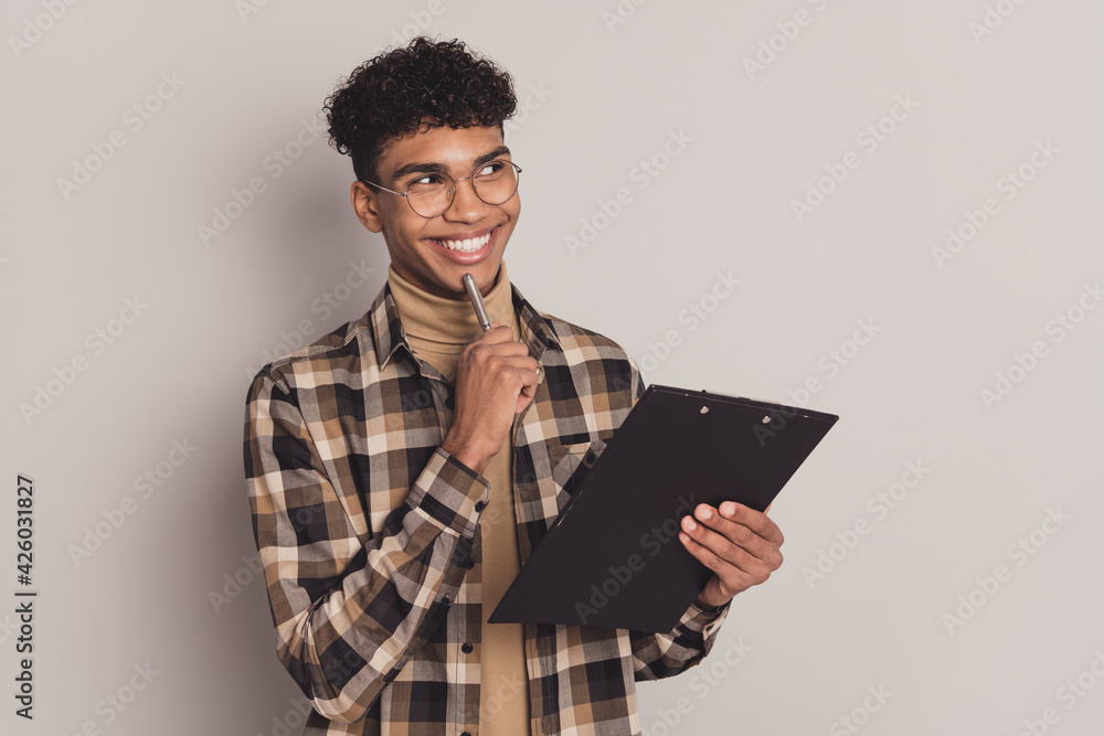 Photo portrait of dreamy curious guy writing exam on clipboard interview looking blank space smiling isolated on grey color background Photo portrait of dreamy curious guy writing exam on clipboard interview looking blank space smiling isolated on grey color background